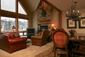 A cozy living room with a fireplace, a television, and a dining area with a chandelier. - Lakota Antlers 200 5 Bedroom Holiday Home by Winter Park Lodging Company (Winter Park)