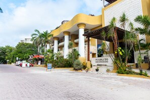 Un hotel con fachada amarilla, palmeras y un cartel que dice "Pueblo Escondido".