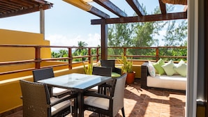 A covered outdoor seating area with wicker furniture, a glass table, and a potted plant.