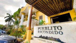 A sign for Pueblo Segundo Condominium Resort with a clear view of the entrance, palm trees, and a yellow building facade.
