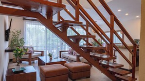 A spacious living area with a wooden staircase, comfortable seating, and a large window providing natural light.