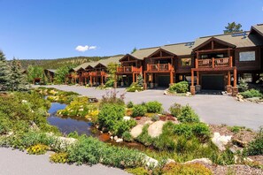 A lodge with multiple wooden buildings, a small stream, and a mountainous backdrop. - Slopeside 202 3 Bedroom Holiday Home by Winter Park Lodging Company (Winter Park)