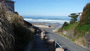 Eine Küstenstraße führt zu einem Strand mit einer Steintreppe und Blick auf das Meer.