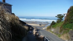 Eine Küstenstraße mit einem Steinhaus links, einem Strand im Hintergrund und einem klaren Himmel.