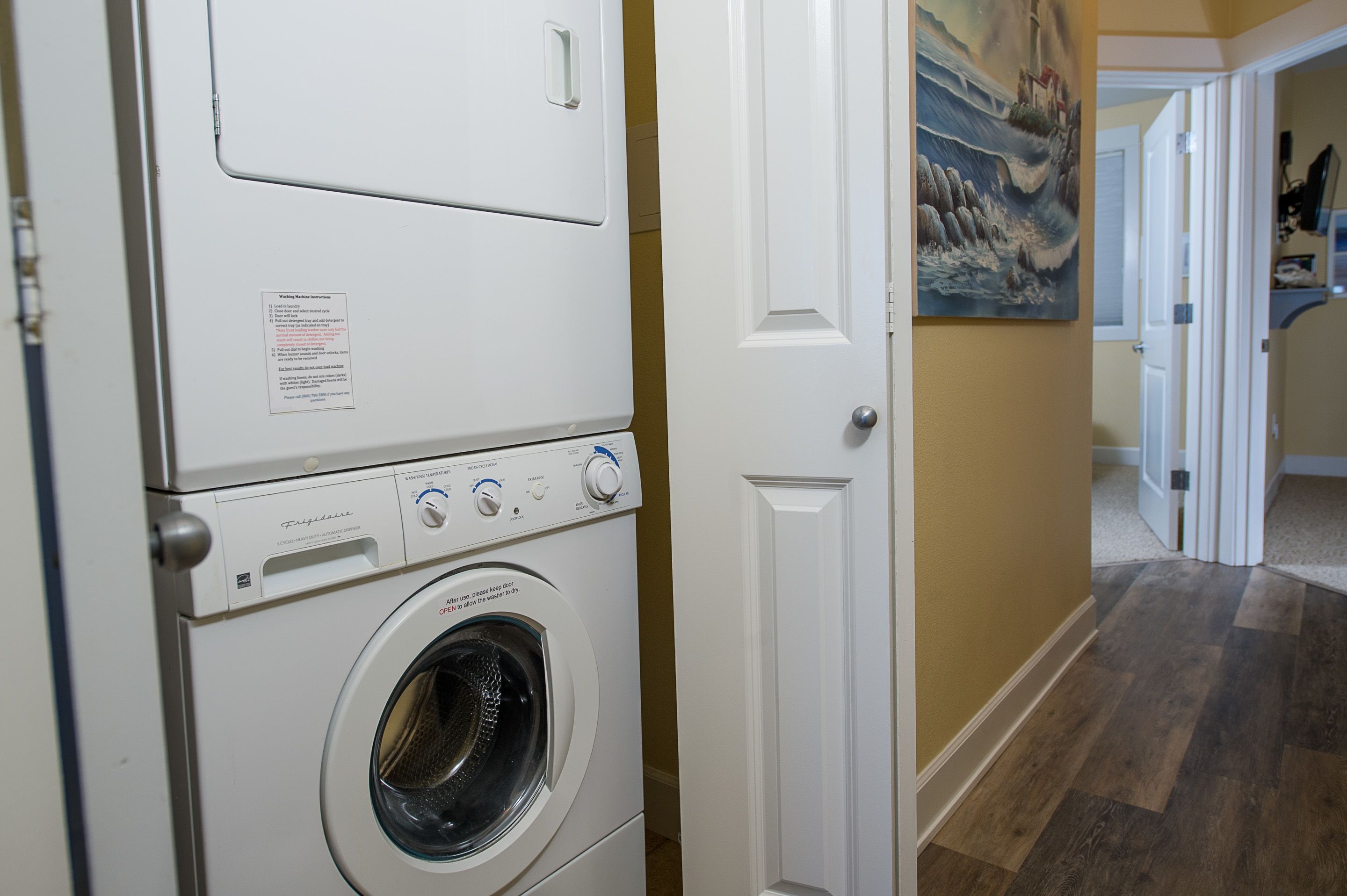 A laundry room with stacked washers and dryers, a door to another room, and a painting on the wall.