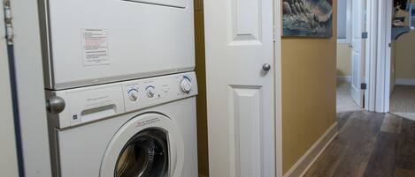 A laundry room with stacked washers and dryers, a door to another room, and a painting on the wall.