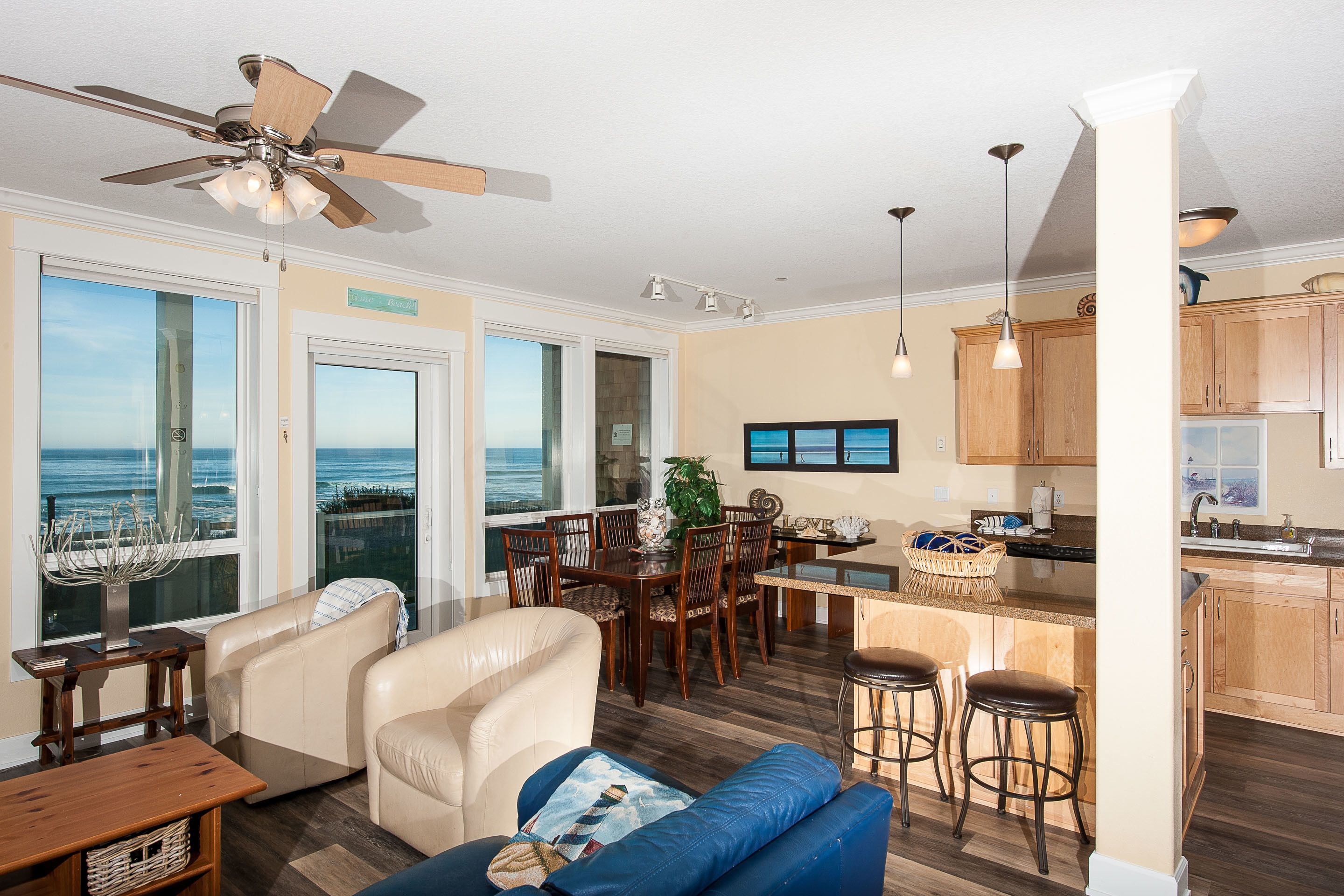 A spacious living area with a dining table, comfortable seating, a kitchen area, and a view of the ocean through large windows.