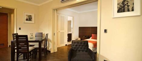 Een hotelkamer met een eethoek, een bed met rode accenten en een zwarte fauteuil.