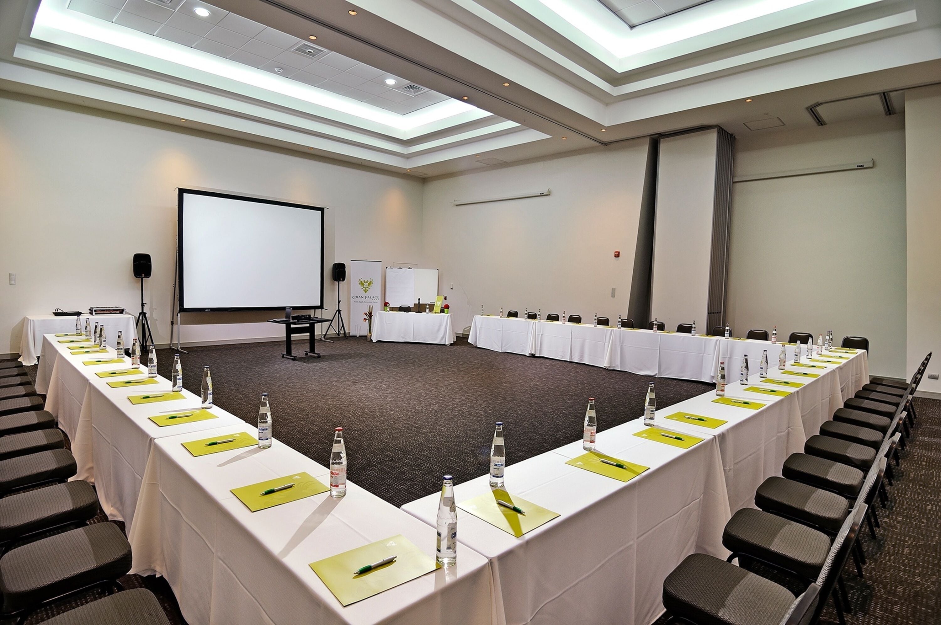 Un salón de conferencias con una larga mesa, sillas, una pantalla de proyector y una pizarra.