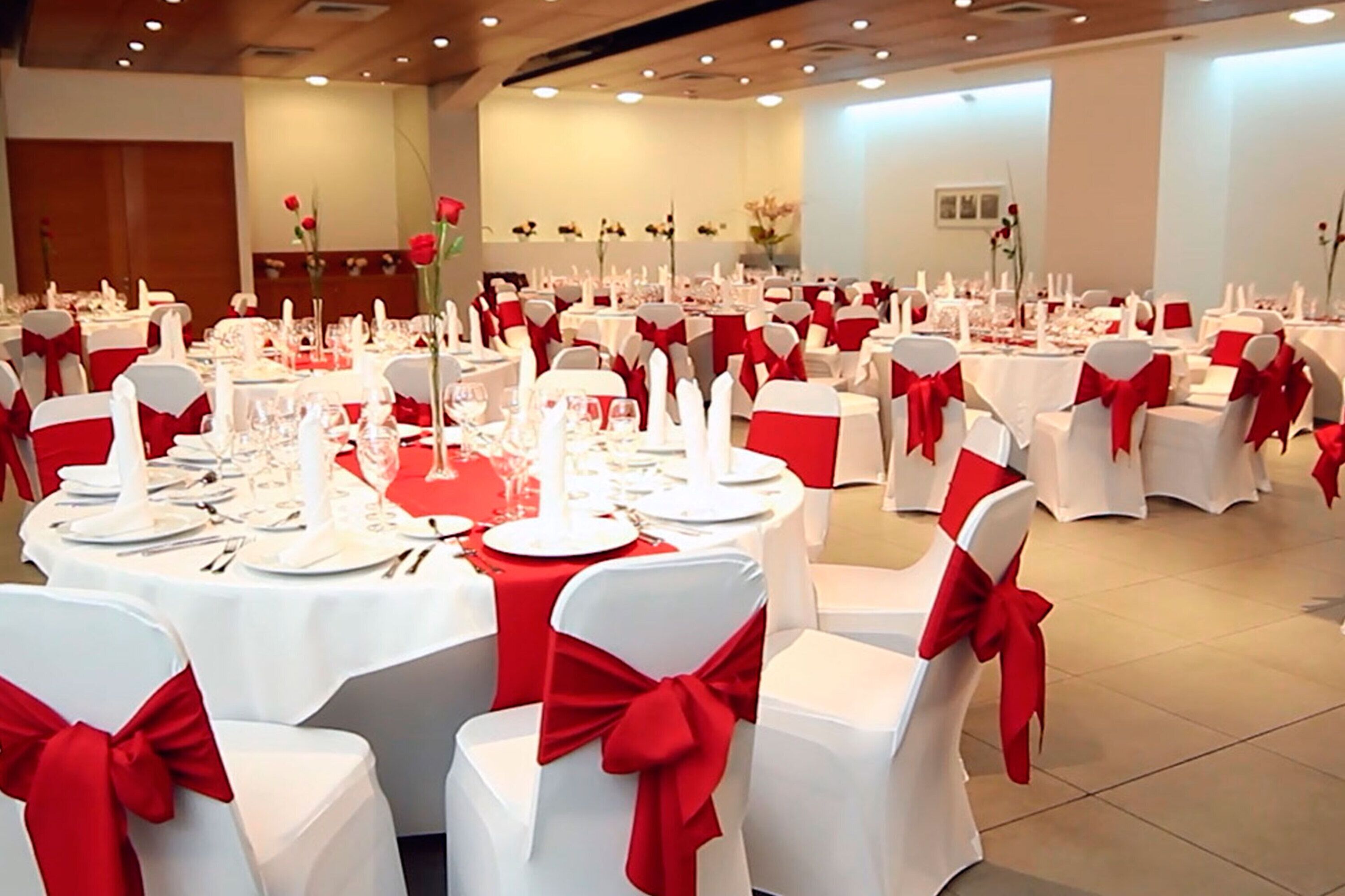 Une salle de banquet avec des tables rondes dressées pour un événement formel, chacune étant recouverte d’une nappe blanche et ornée d’un ruban rouge.