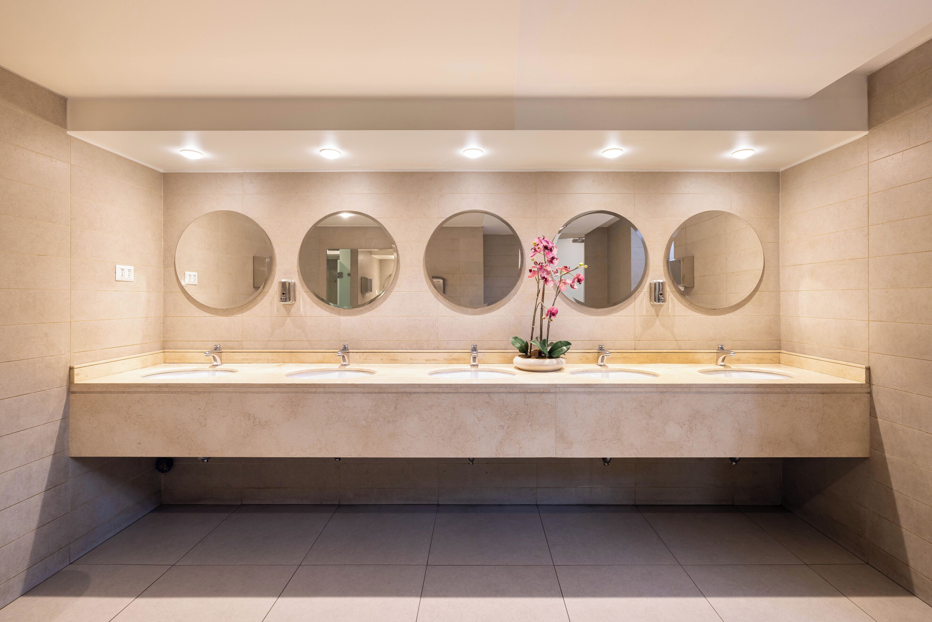 Un bagno moderno con tre lavabi, diversi specchi e un'orchidea in vaso.