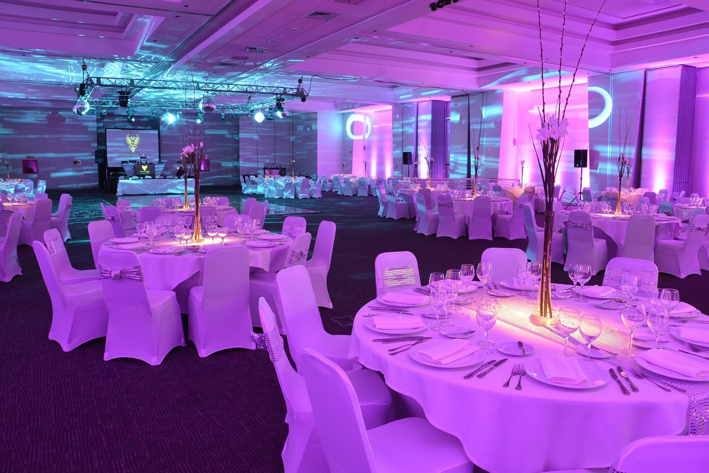 A banquet hall with round tables set for dining, white chairs, and a stage with a podium.