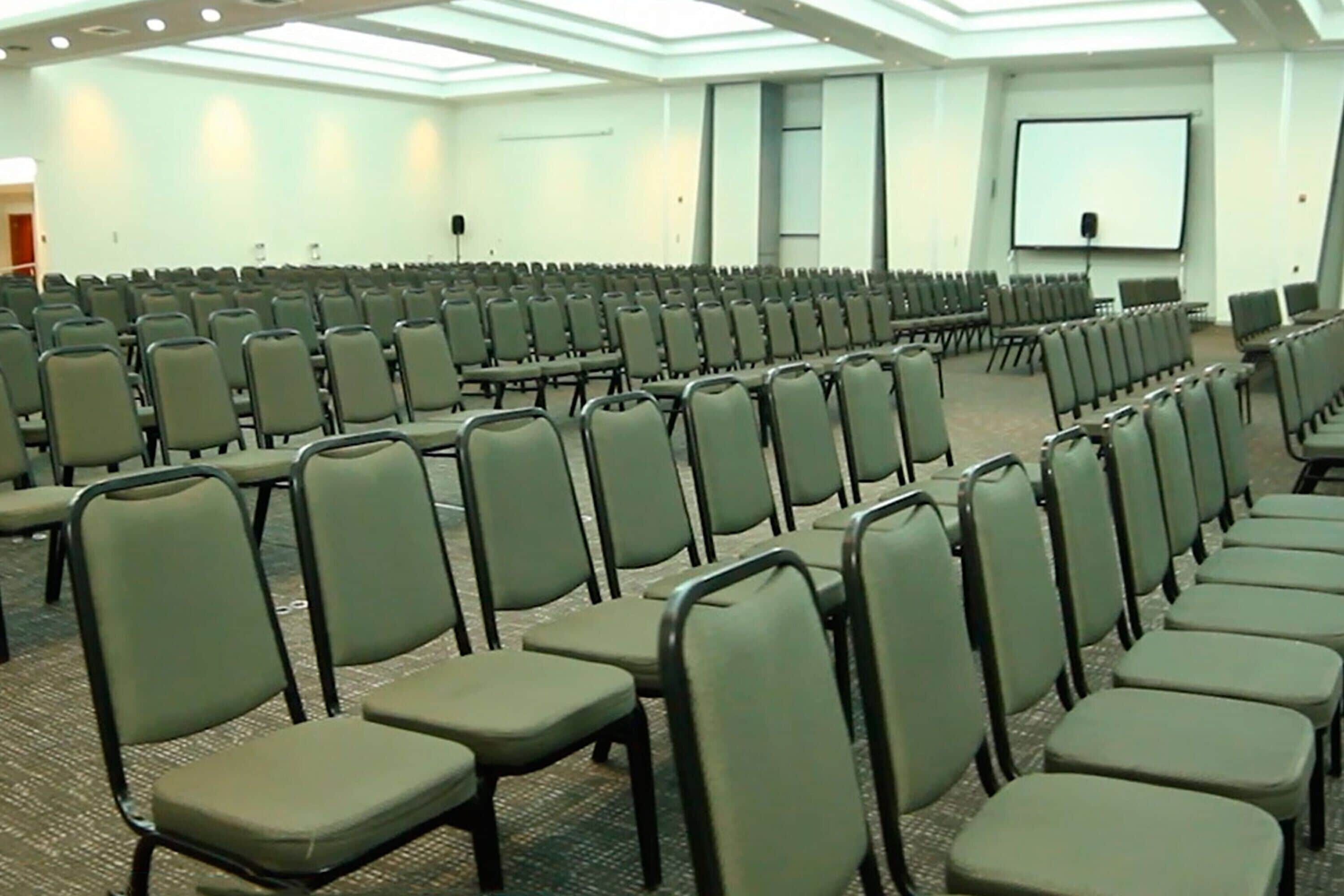 A large conference room with rows of chairs, a projector screen, and a carpeted floor.