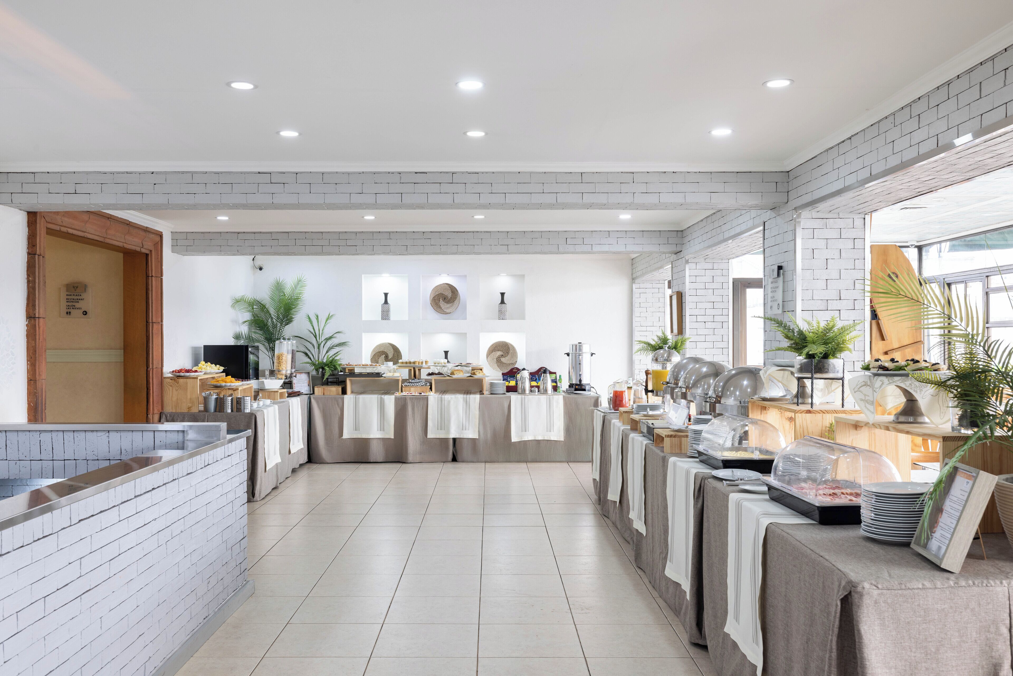 A modern breakfast area with a brick wall, white ceiling, and a variety of breakfast items on tables.