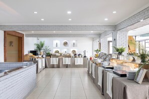 A modern kitchen with white brick walls, recessed lighting, and a long counter with various food items and appliances. - Hotel Gran Palace (Santiago)