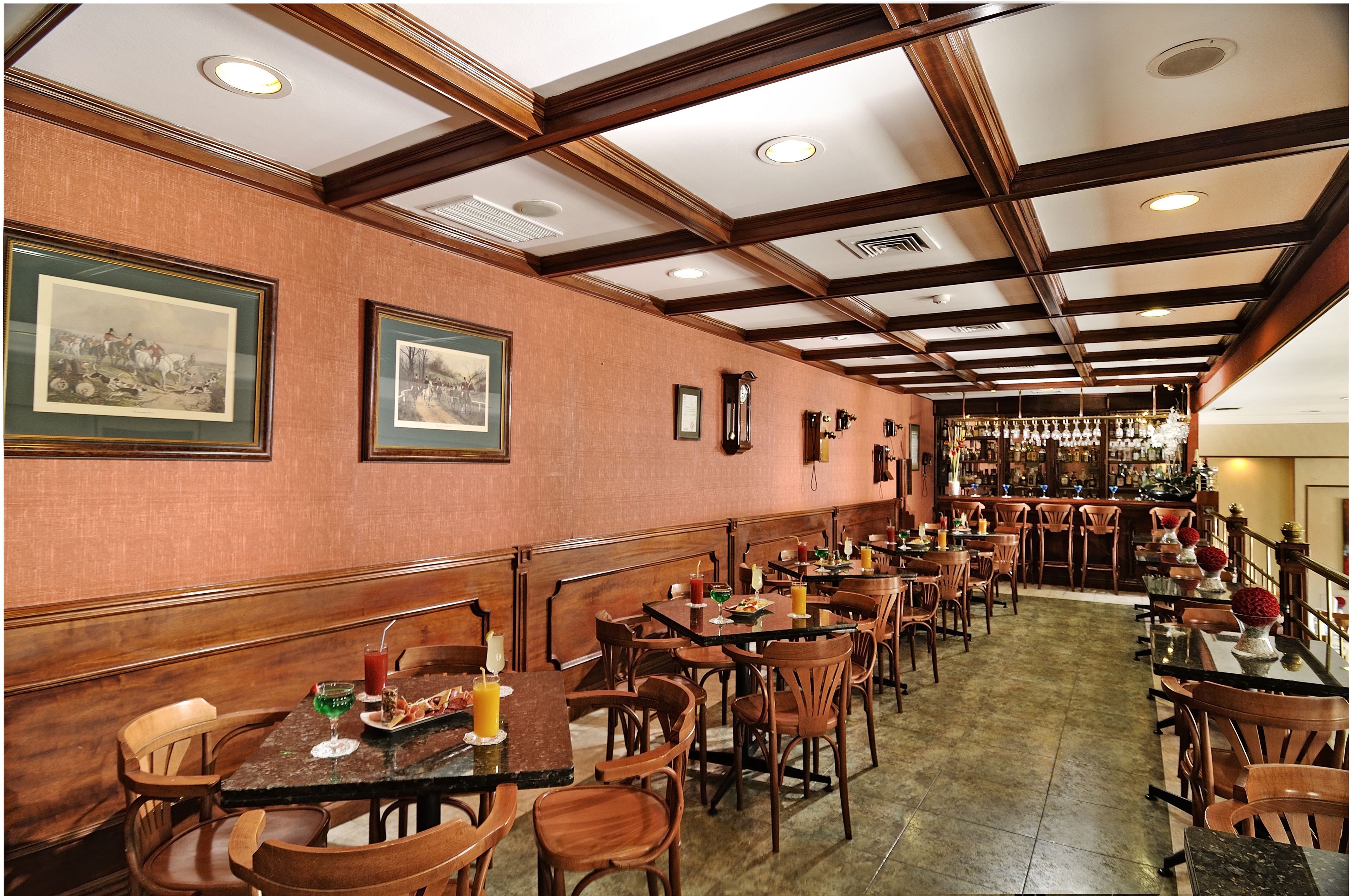 Un restaurante con cabinas y mesas de madera, cuadros en las paredes y un bar al fondo.