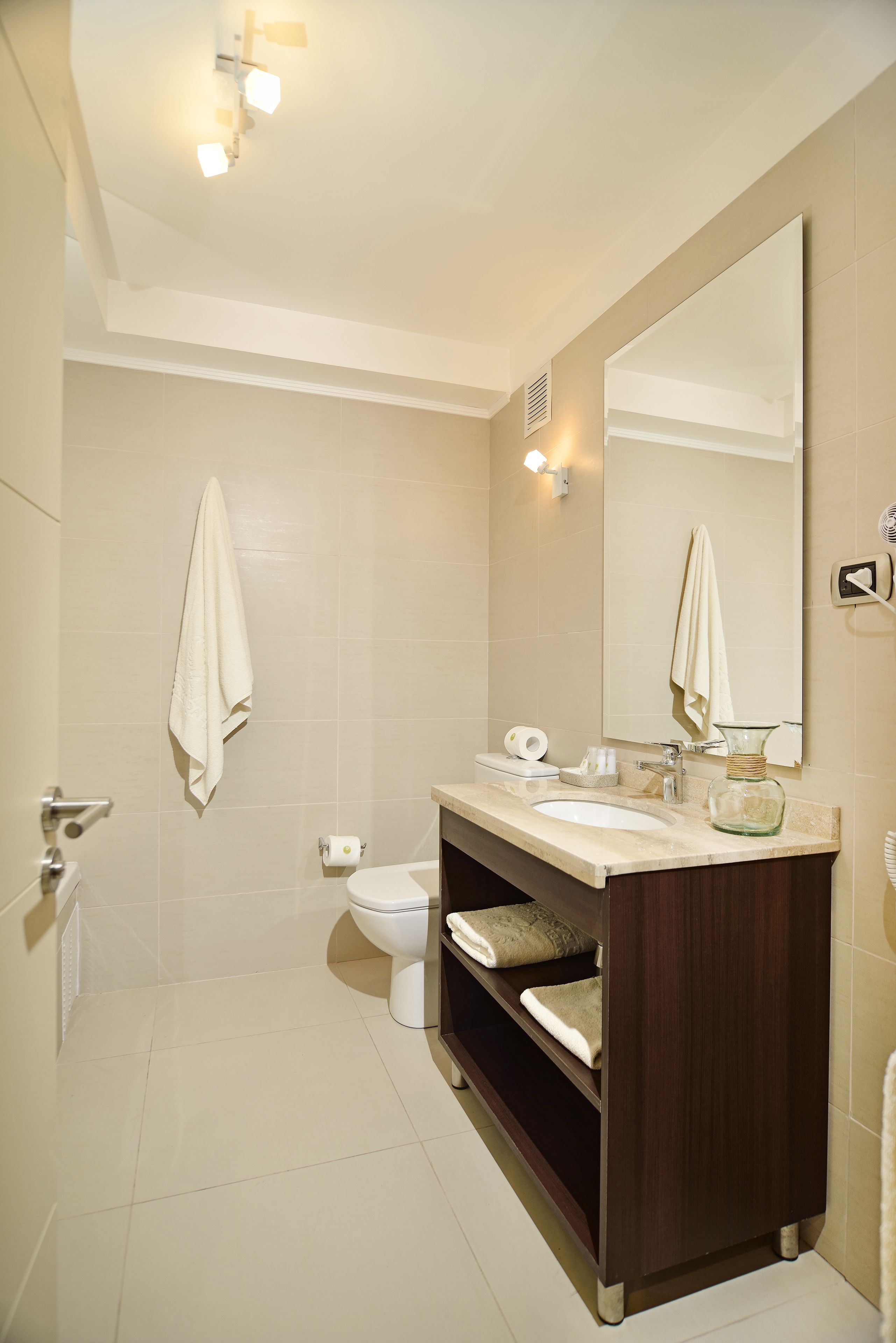 A bathroom with a large mirror, a sink, a toilet, and a towel hanging on the wall.