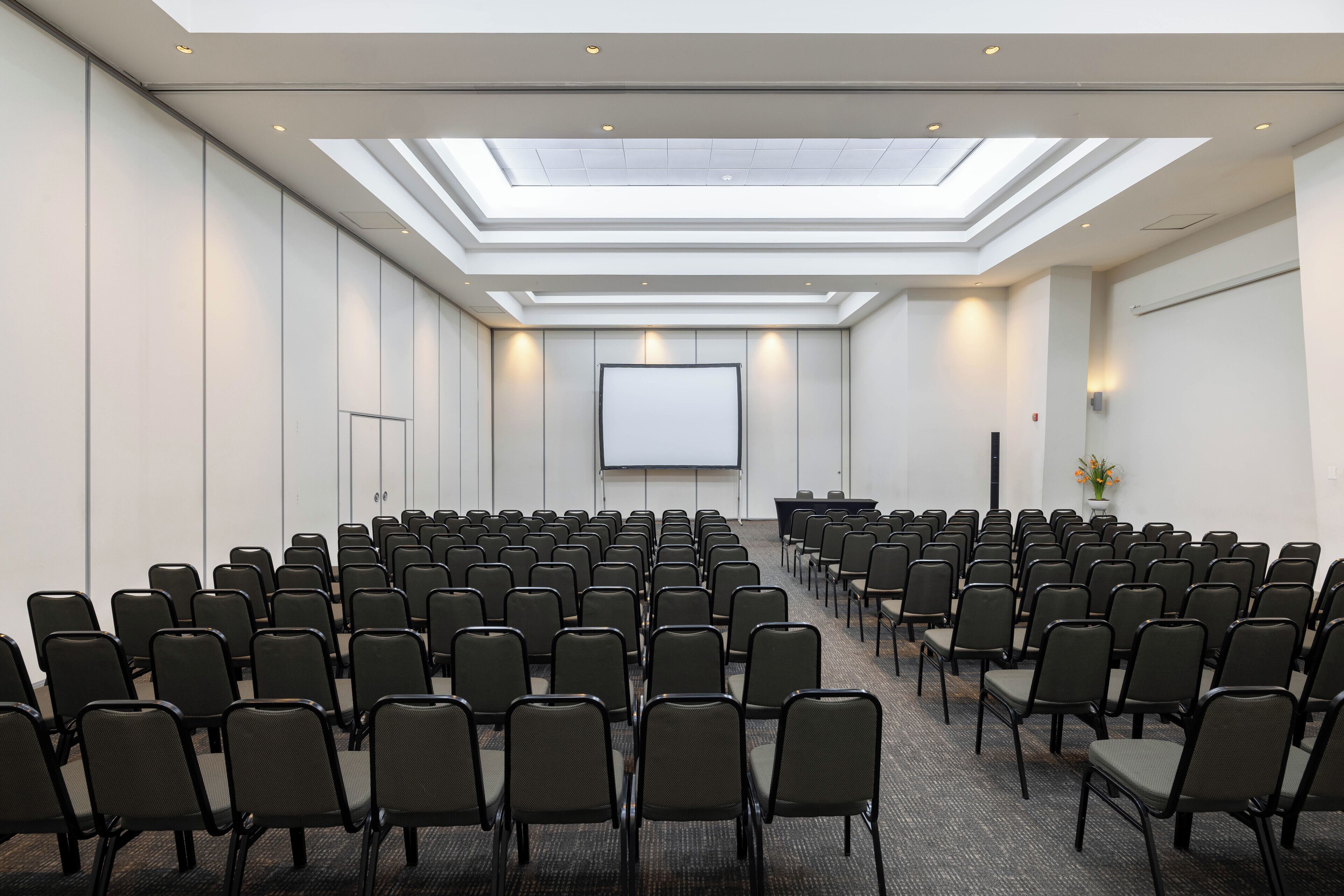 Ein Konferenzraum mit Reihen von Stühlen, einer großen Leinwand und einem Oberlicht.