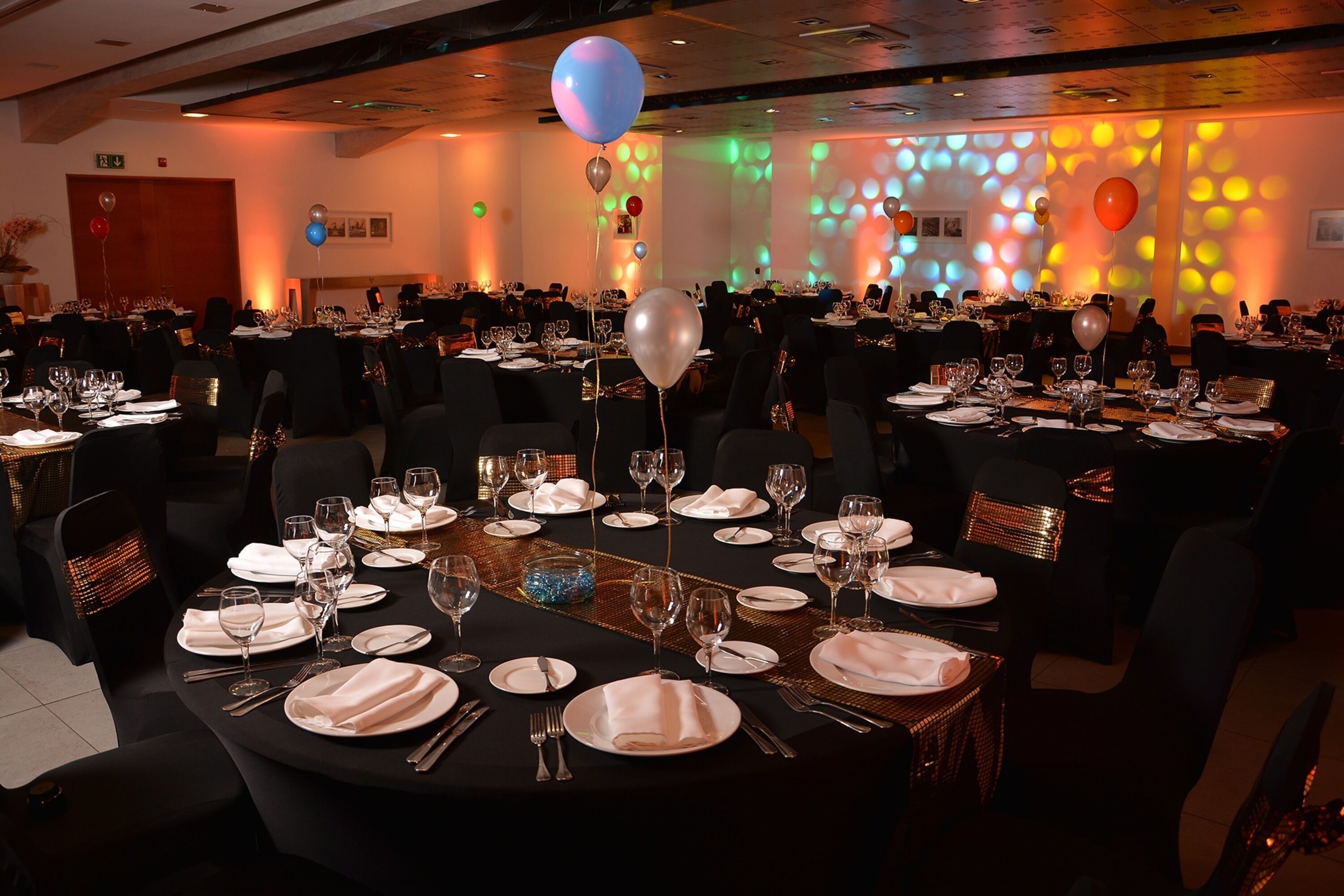 Une salle de banquet avec des tables rondes dressées pour le repas, chacune étant recouverte d’une nappe blanche et agrémentée d’assiettes et de couverts.
