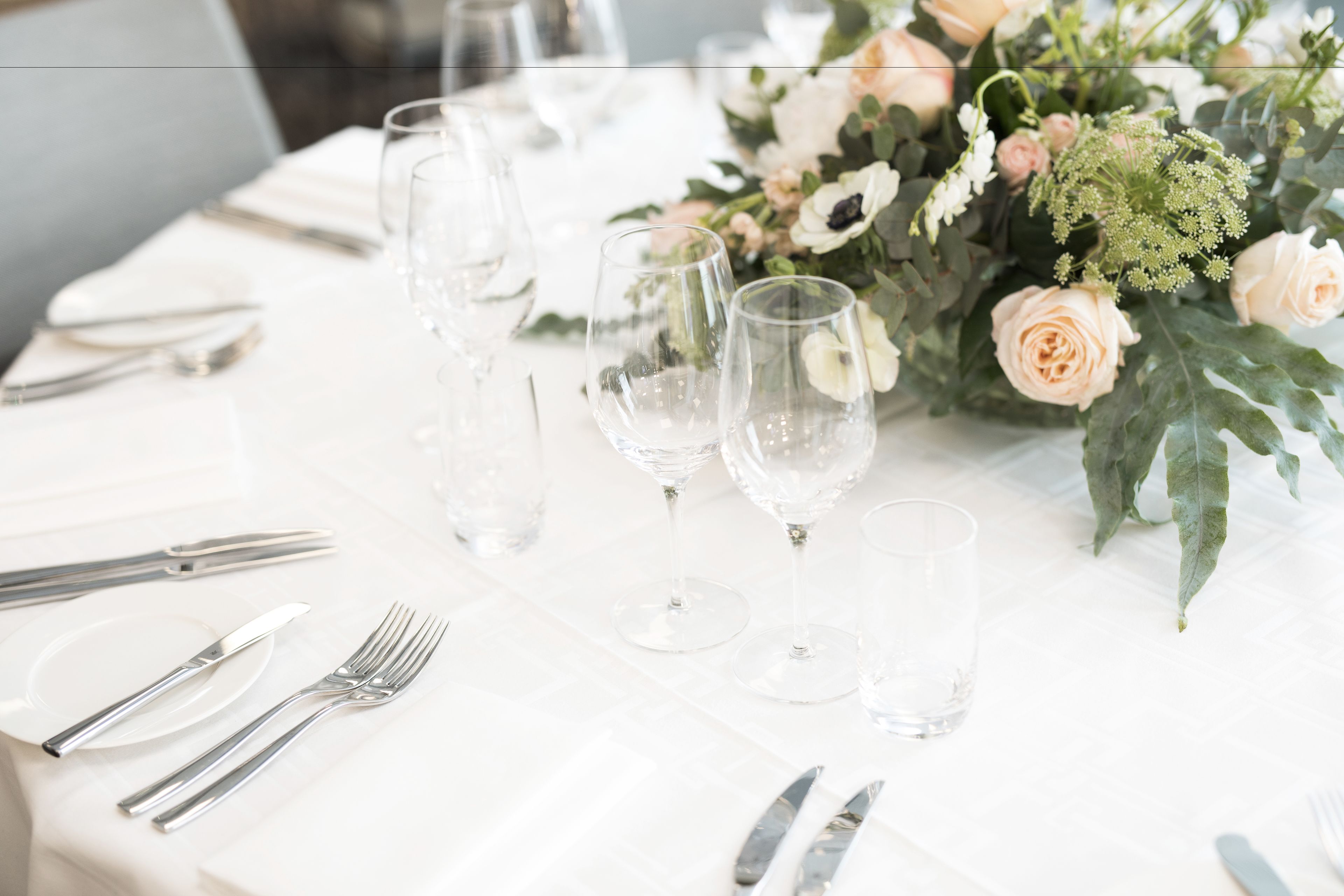 Una mesa dispuesta para un evento formal, con cristalería transparente, cubertería y un centro de mesa floral.