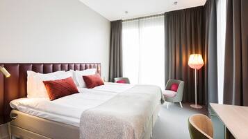 A hotel room with a large bed, two bedside tables, a desk, a chair, and a floor lamp.
