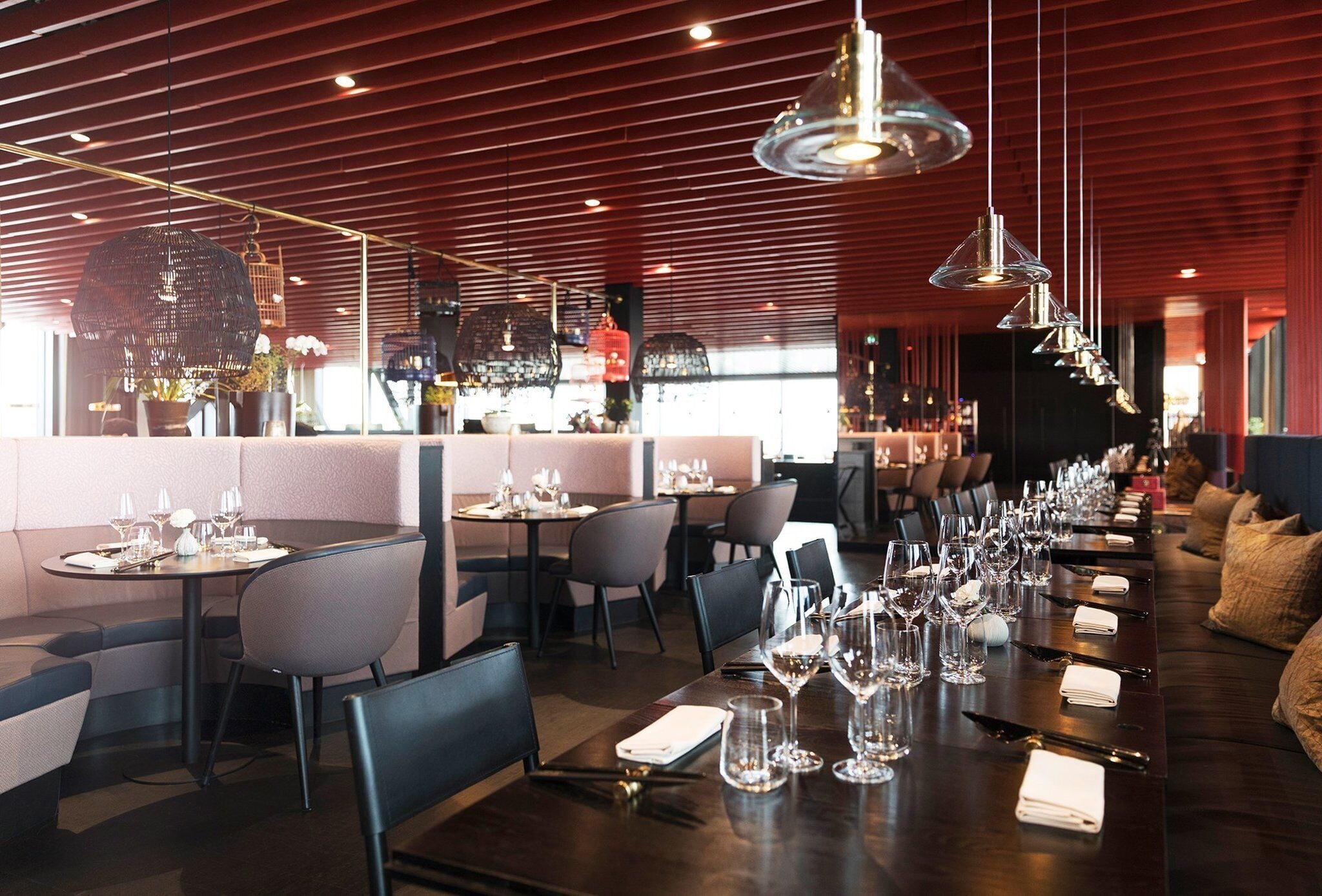 En restaurang med flera matbord, dukade med vinglas och bestick, en bardisk i bakgrunden och en modern takdesign.