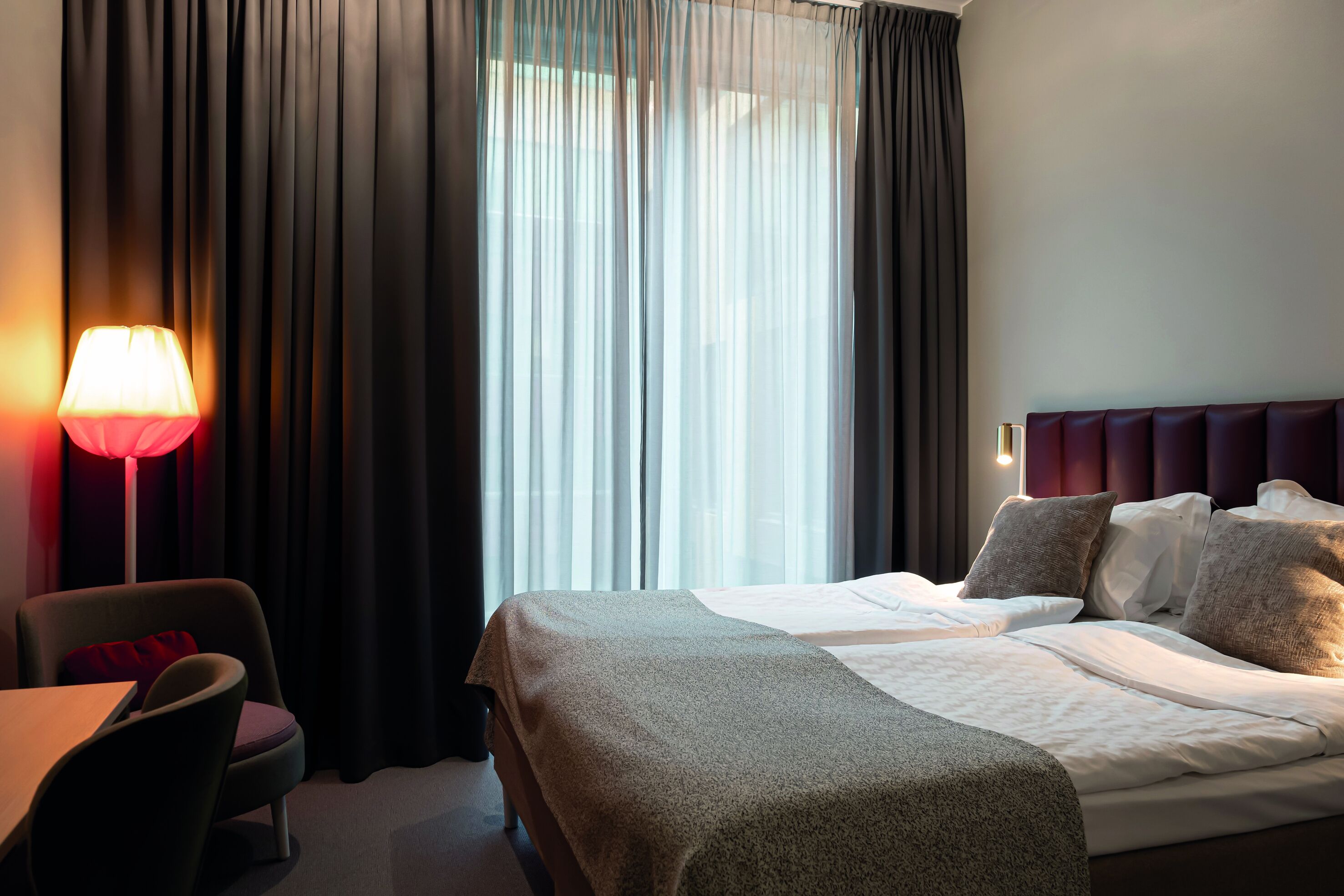 Una habitación de hotel con una cama, una silla, un escritorio y una lámpara.
