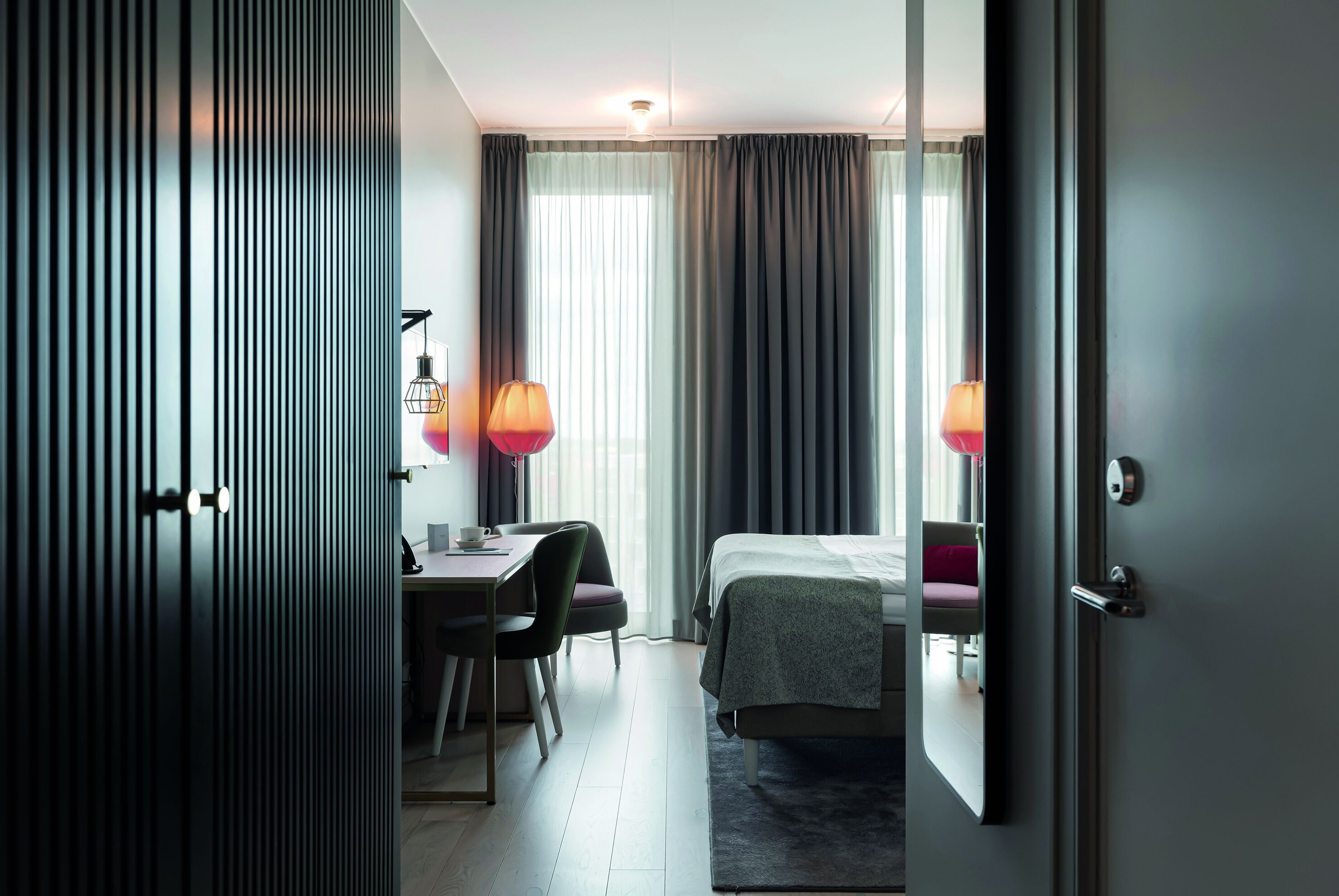 A hotel room with a bed, a desk, two chairs, and a lamp.
