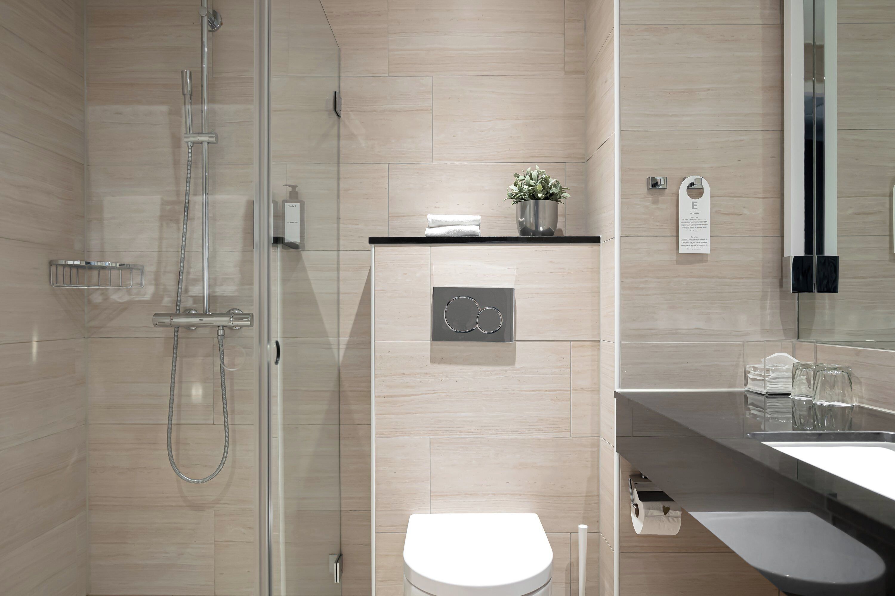 A modern bathroom with a glass-enclosed shower, a white toilet, and a black countertop with a sink and a small potted plant.