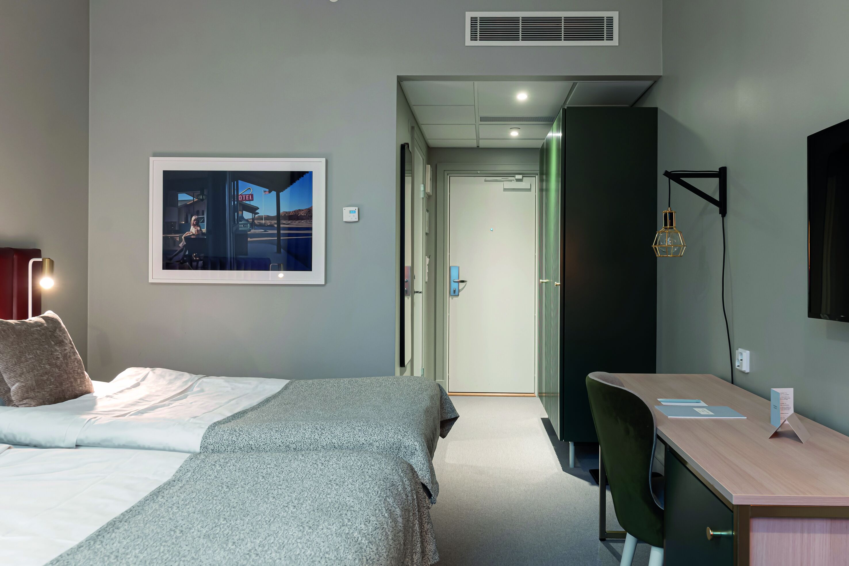 Ein Hotelzimmer mit einem Bett, einem Schreibtisch und einem Stuhl. An der Wand hängt ein Bild und das Fenster bietet einen Blick auf ein Gebäude.