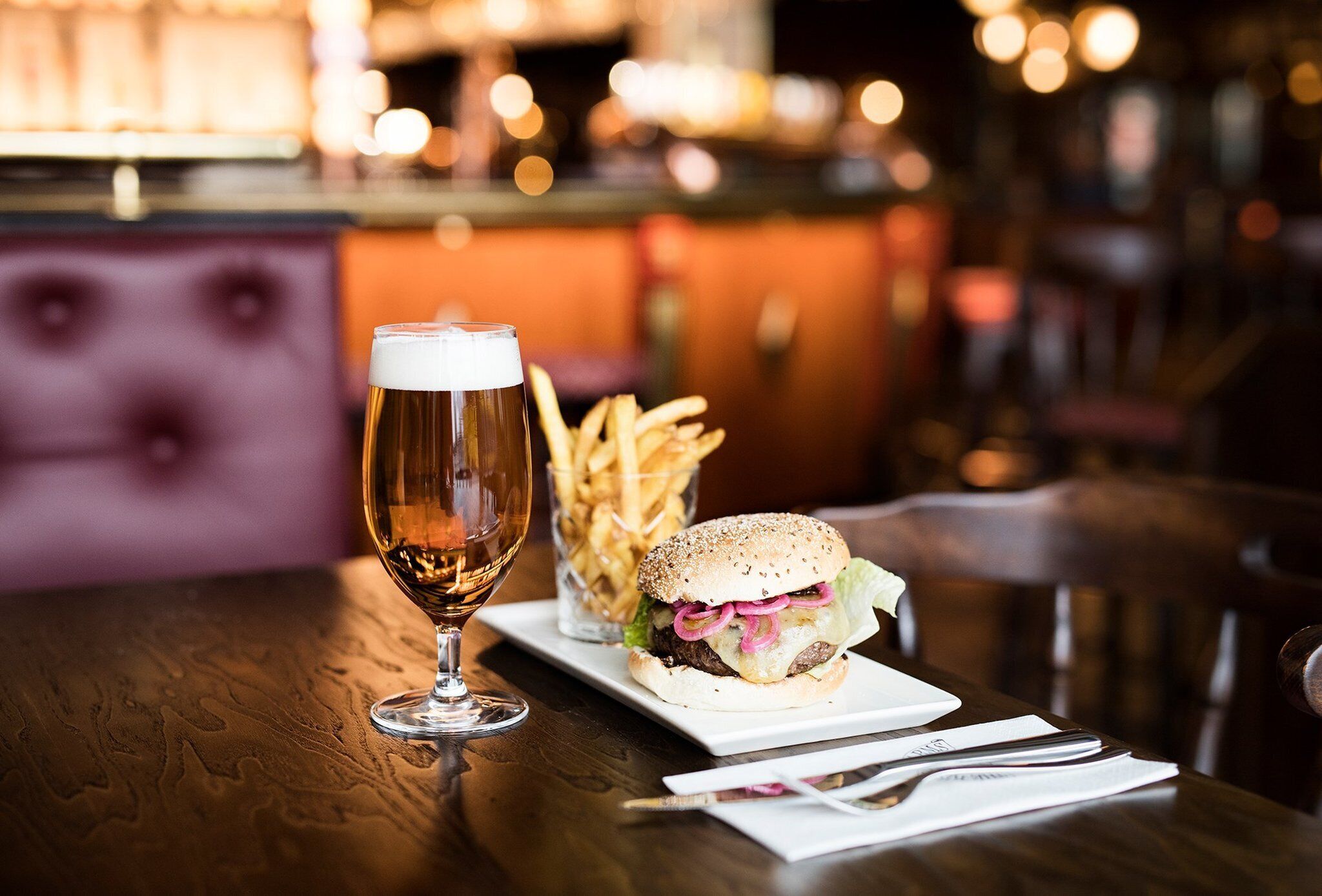 A dining table with a beer glass, a burger, and a container of fries.