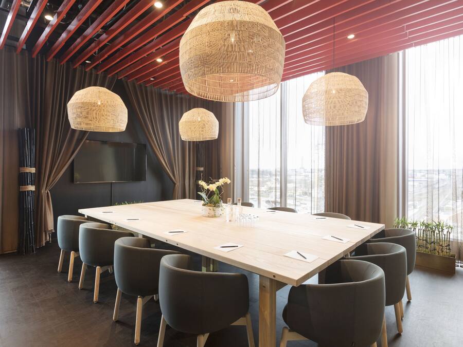 A conference room with a large table, multiple chairs, and three large hanging lamps.