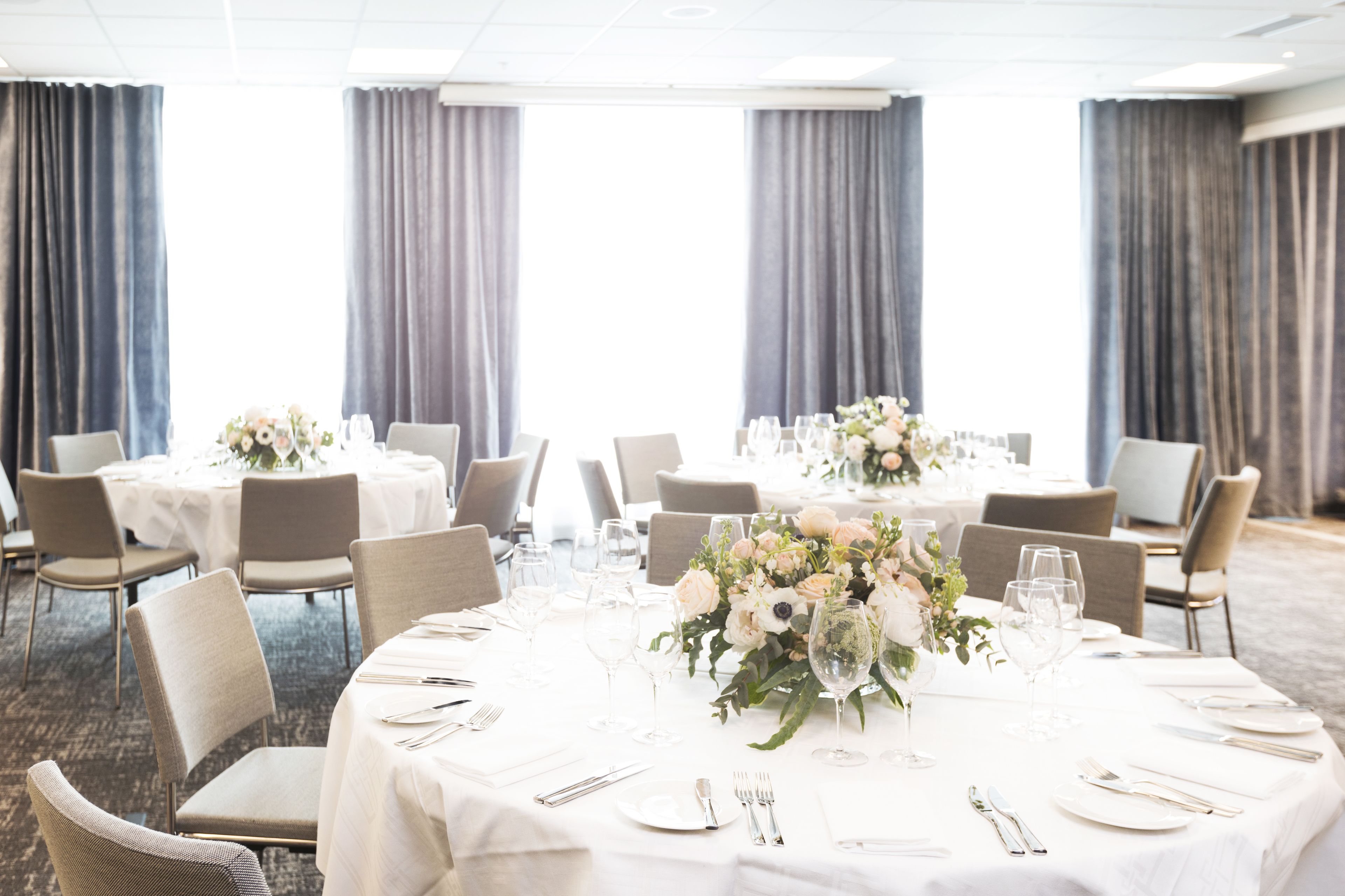 A banquet hall with round tables set for dining, featuring white tablecloths, chairs, and floral centerpieces.