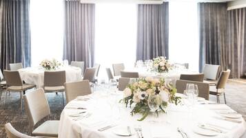 A banquet hall with round tables set for dining, featuring white tablecloths, chairs, and floral centerpieces.