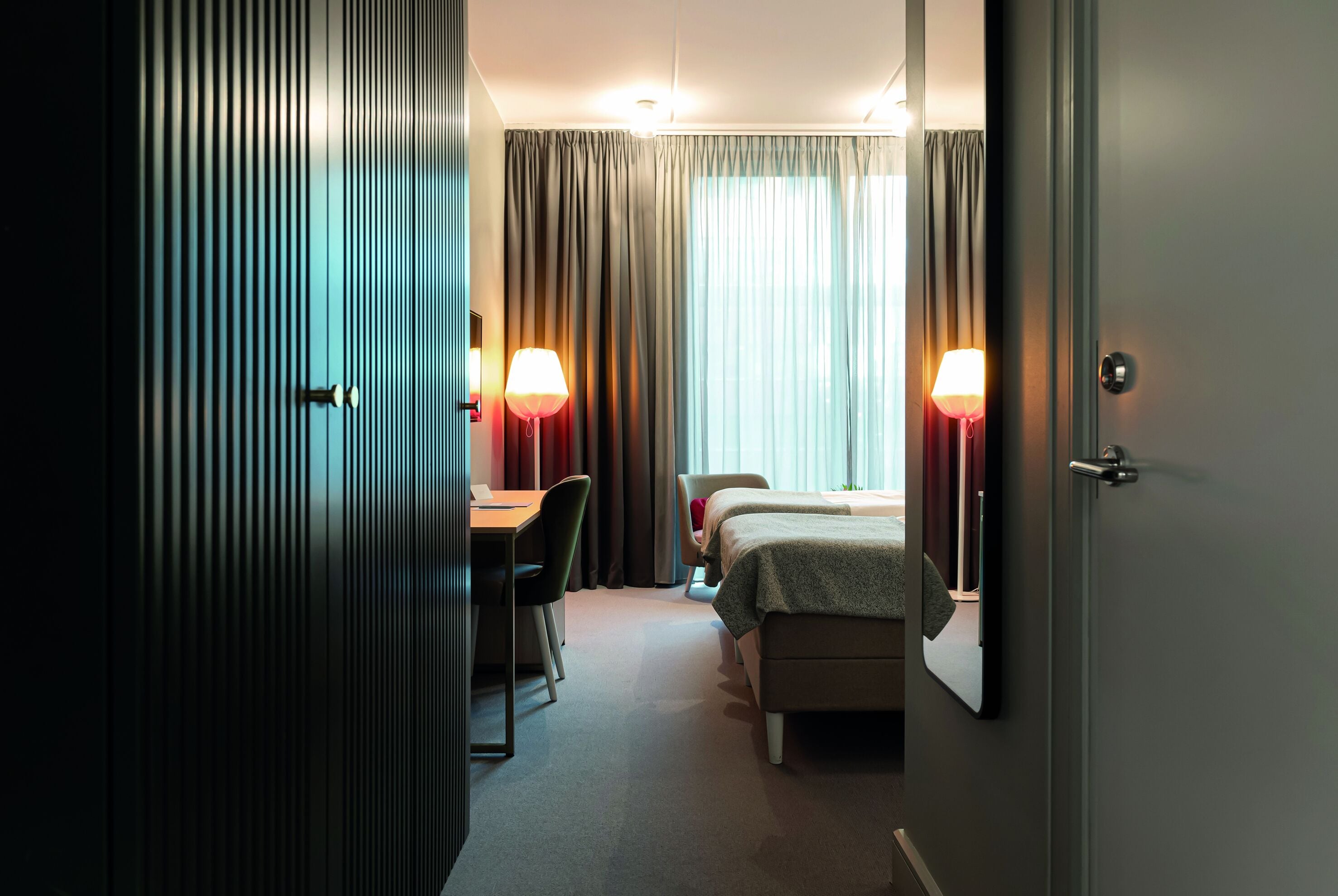 Une chambre d’hôtel avec un bureau, deux lits et deux lampes.