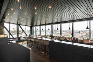 A modern bar with a high ceiling, large windows, and a city view. - Elite Hotel Academia (Uppsala)