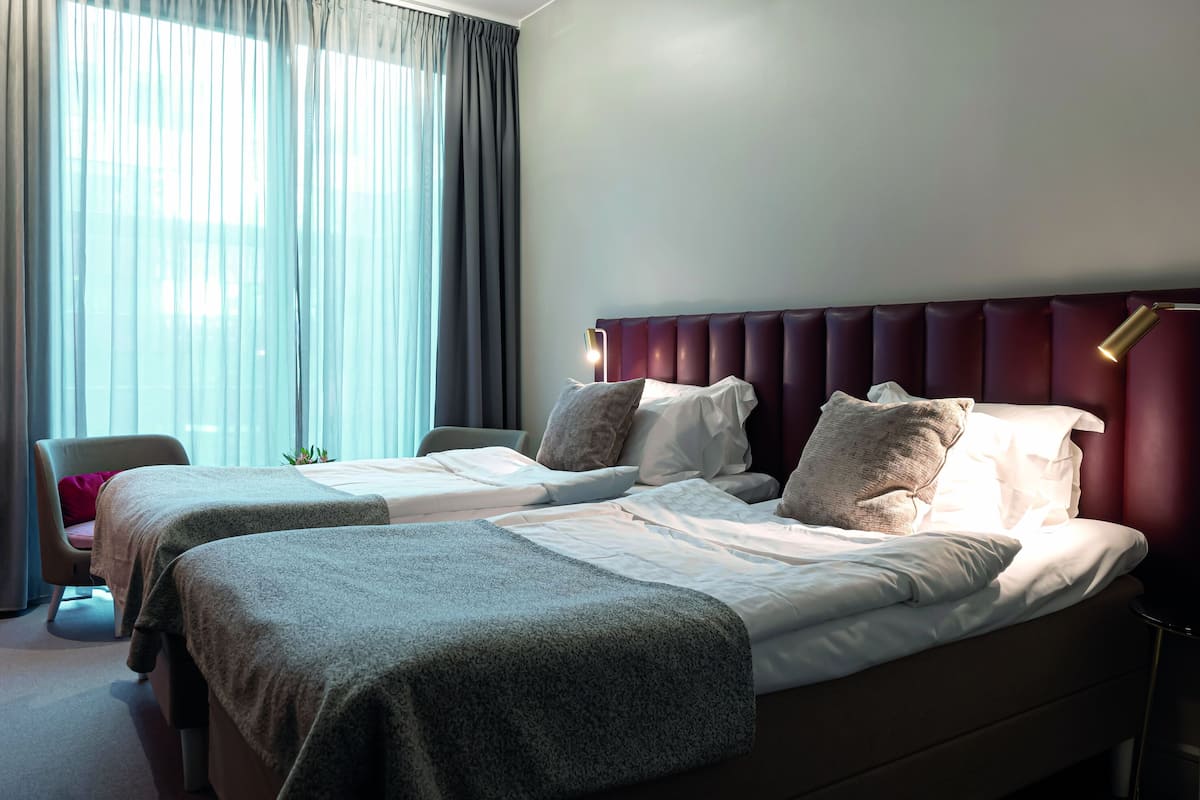 A hotel room with two beds, a chair, a bedside table, and a lamp.