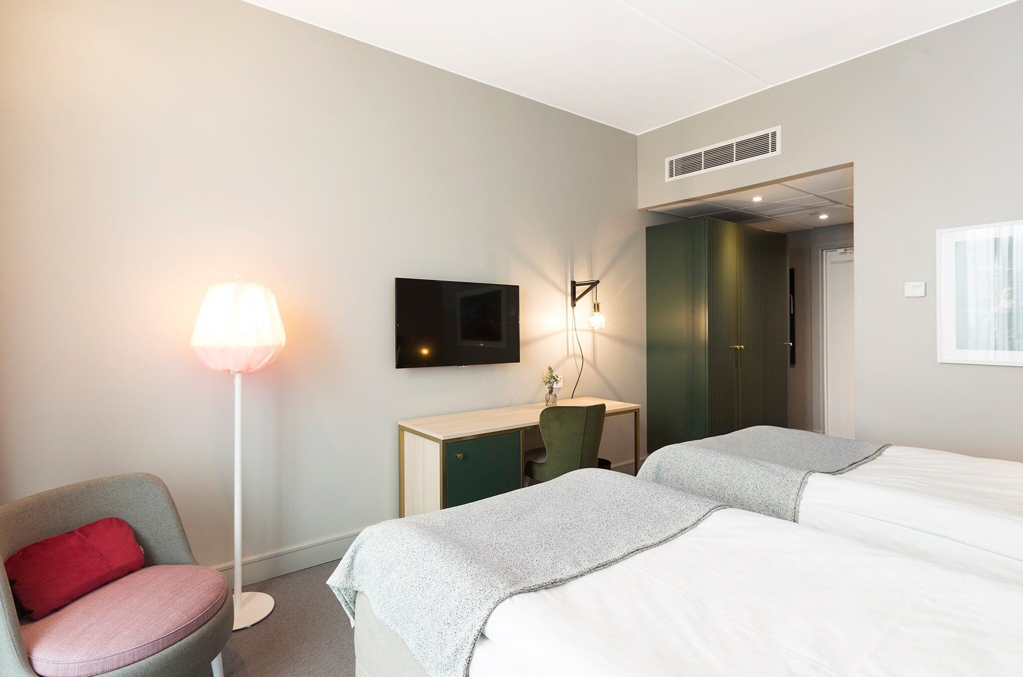Ein Hotelzimmer mit zwei Betten, einem Schreibtisch, einem Sessel, einem Fernseher und einer Lampe.