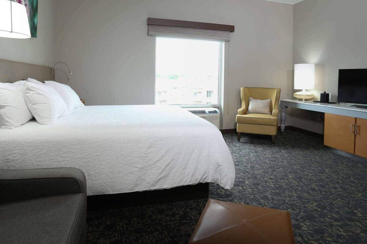 Ein Hotelzimmer mit Bett, Sessel, Schreibtisch, Fernseher und Fenster.