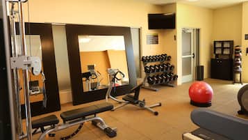 A gym with exercise equipment, a mirror, a television, and a wall-mounted rack of dumbbells.