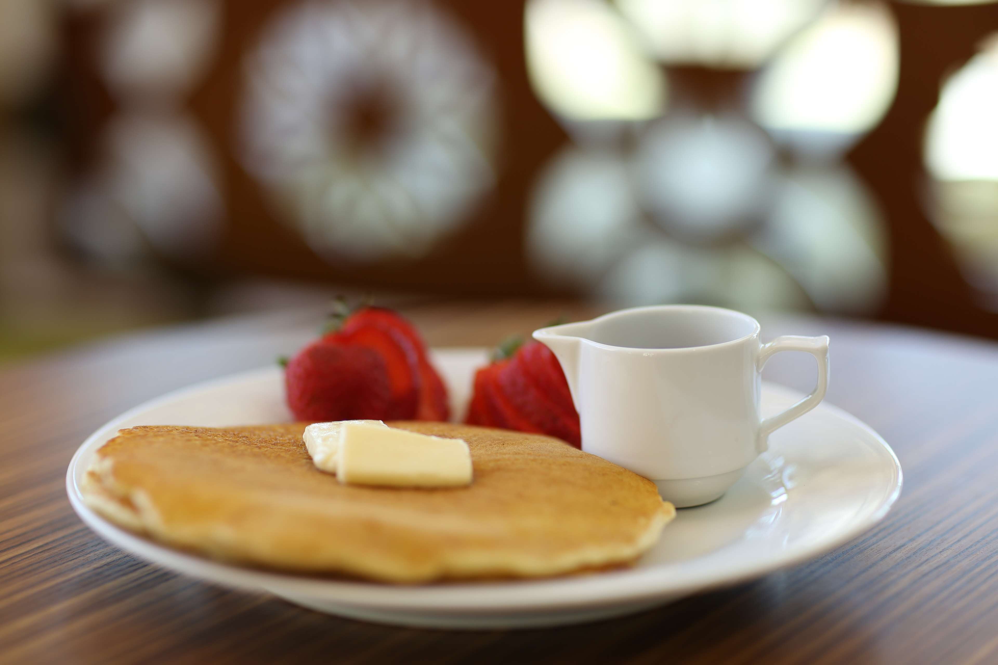 A plate with pancakes, butter, and strawberries on a wooden table.