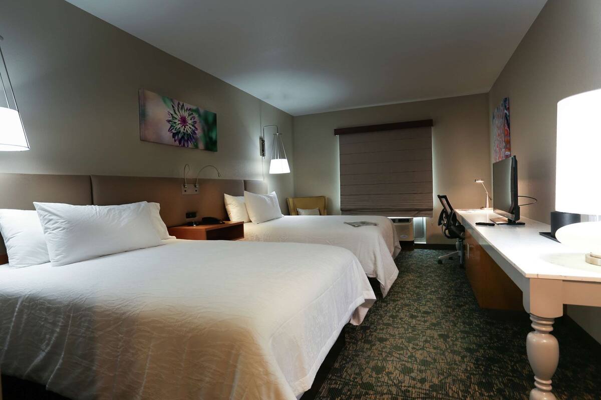 Ein Hotelzimmer mit zwei Betten, einem Schreibtisch, einem Stuhl, einer Lampe und einem Fernseher.