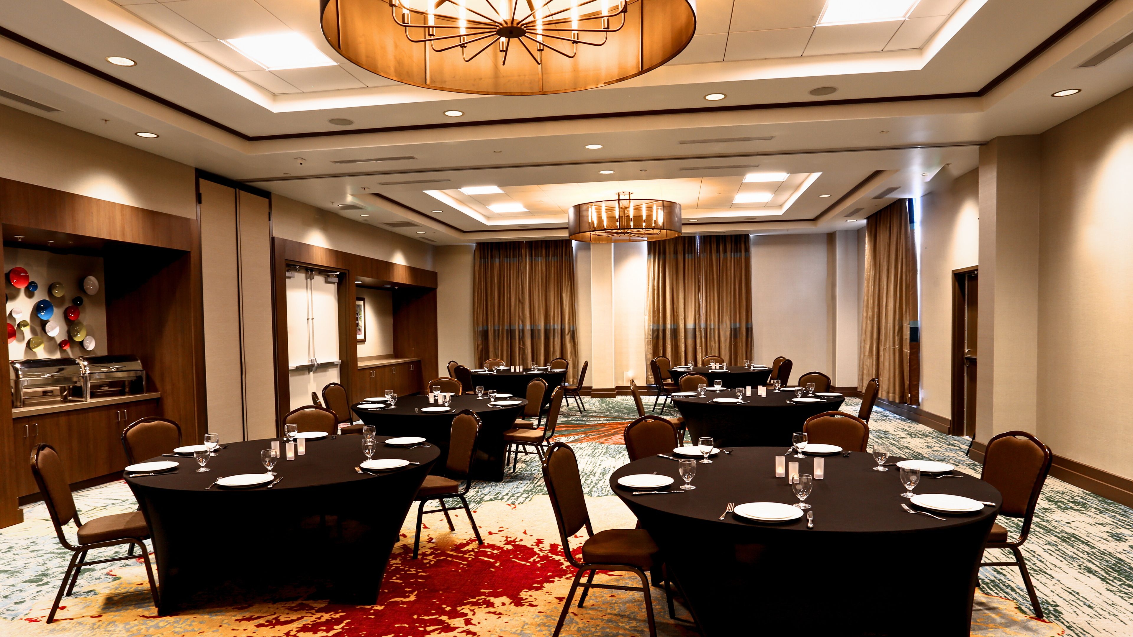 A conference room with multiple tables, chairs, and a buffet area with a variety of glassware.