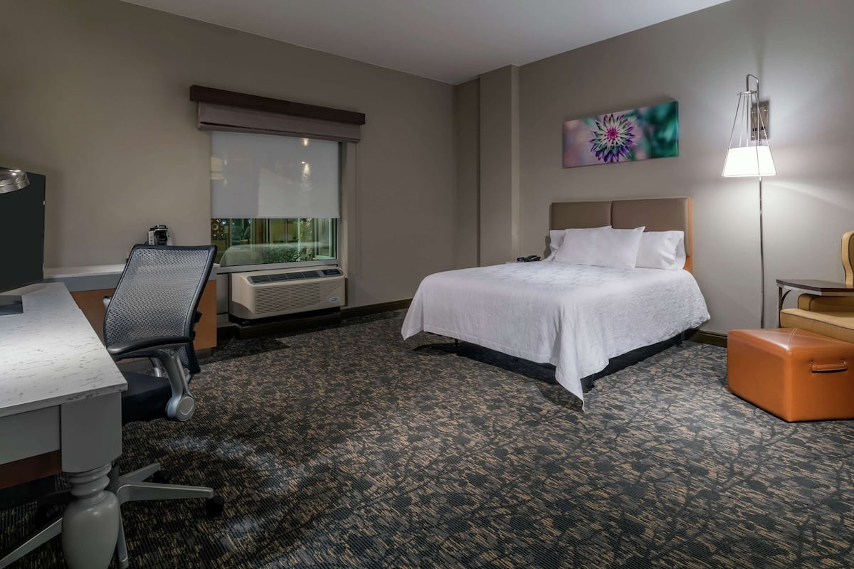 Ein Hotelzimmer mit Bett, Schreibtisch, Stuhl, Klimaanlage und einem Fenster mit Jalousien.