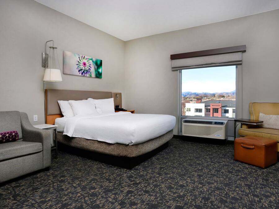 A hotel room with a bed, a sofa, a chair, a table, and a window with a view.