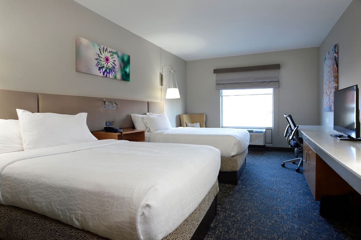 Ein Hotelzimmer mit zwei Betten, einem Schreibtisch mit Fernseher, einer Lampe und Bildern an den Wänden.