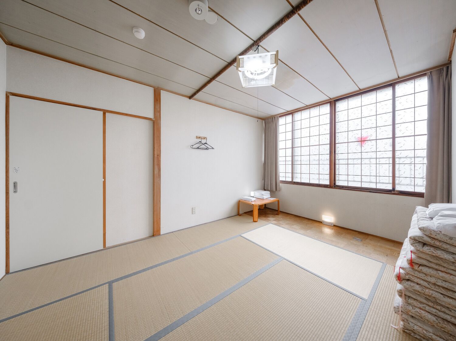 Une pièce traditionnelle japonaise avec un sol recouvert de tatamis, des portes coulissantes, une petite table et un lit avec une literie soigneusement pliée.