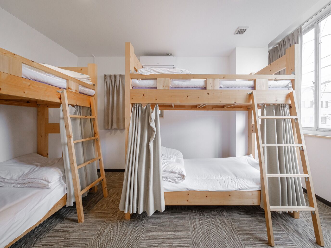 Une chambre de dortoir avec des lits superposés, des échelles en bois et une fenêtre avec des rideaux.