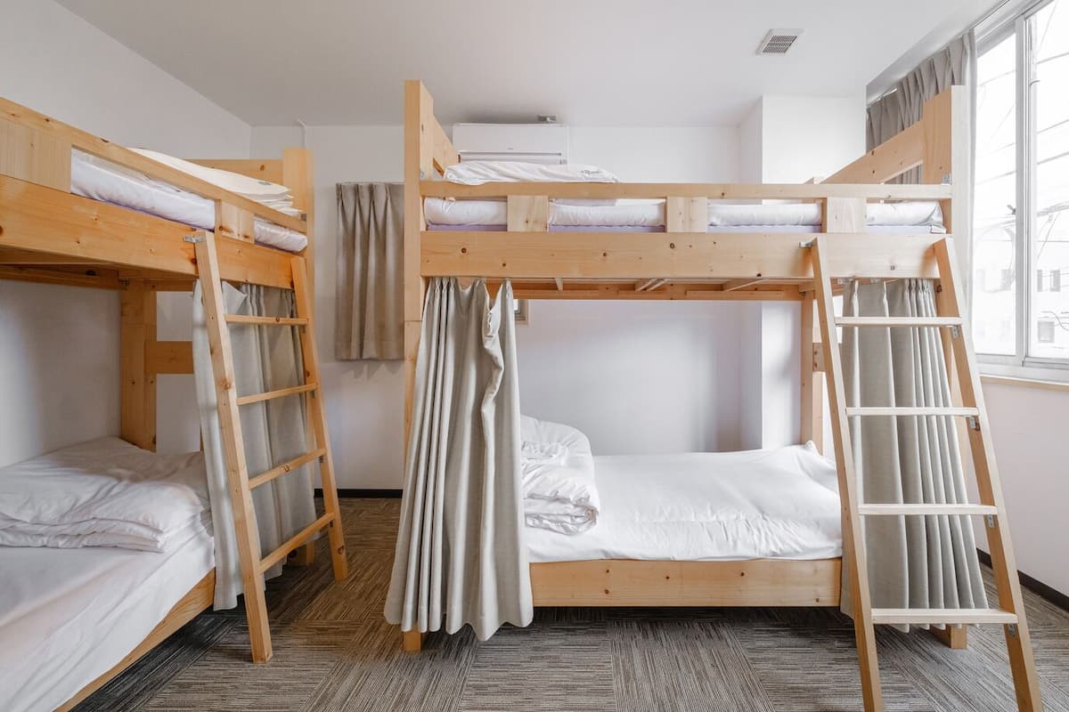 A dormitory room with bunk beds, wooden ladders, and a window with curtains.
