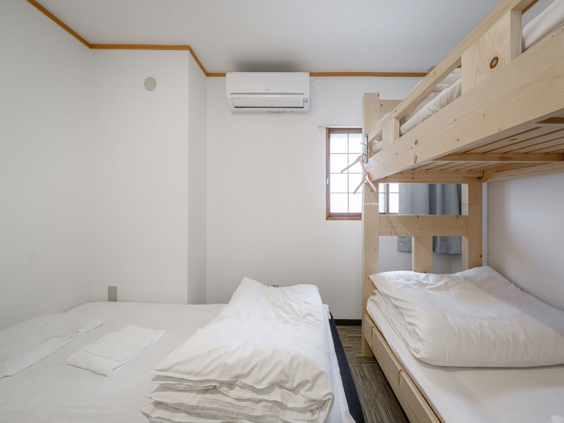 Une chambre avec un lit superposé, un lit simple et une fenêtre.